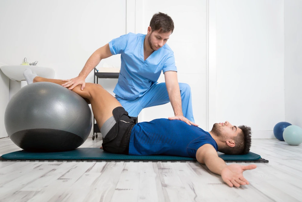 fisio ayudando a un hombre tumbado a hacer un ejercico